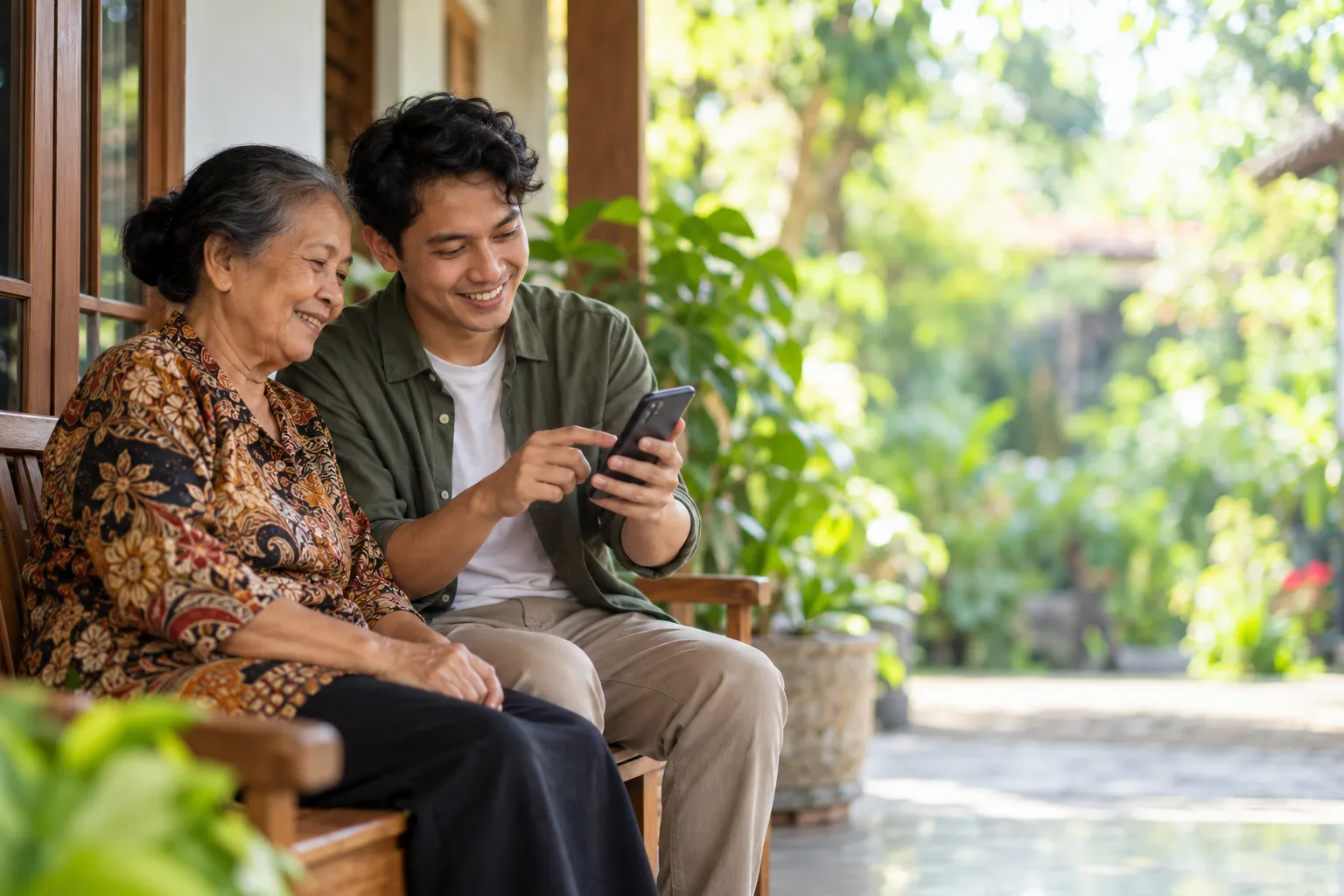 Nenek berbaju batik tersenyum saat cucunya menunjukkan sesuatu di ponsel